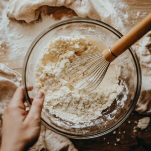 A medium bowl containing whisked all-purpose flour, baking soda, and salt for toll house cookie recipes, with a whisk resting inside.