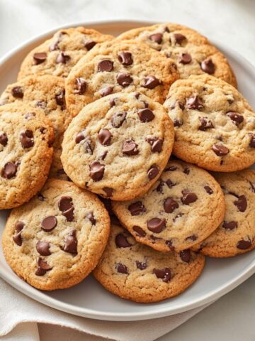 A batch of warm toll house cookies with melted chocolate chips on a cooling rack