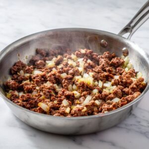 brown the meat for rotel dip recipe with ground beef, garlic, and onion cooking in a pot