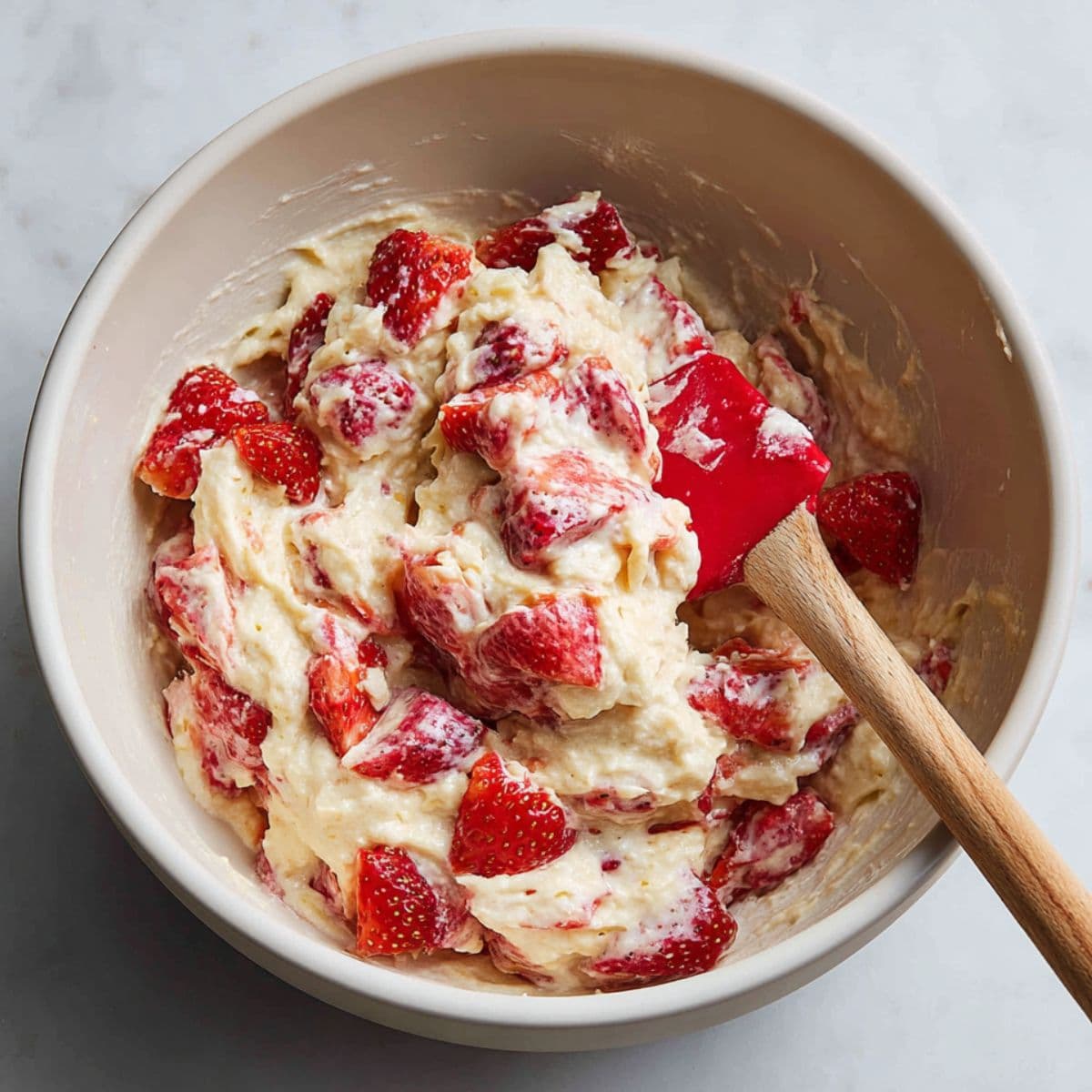 folding chopped strawberries into waffle batter for strawberry waffles recipe