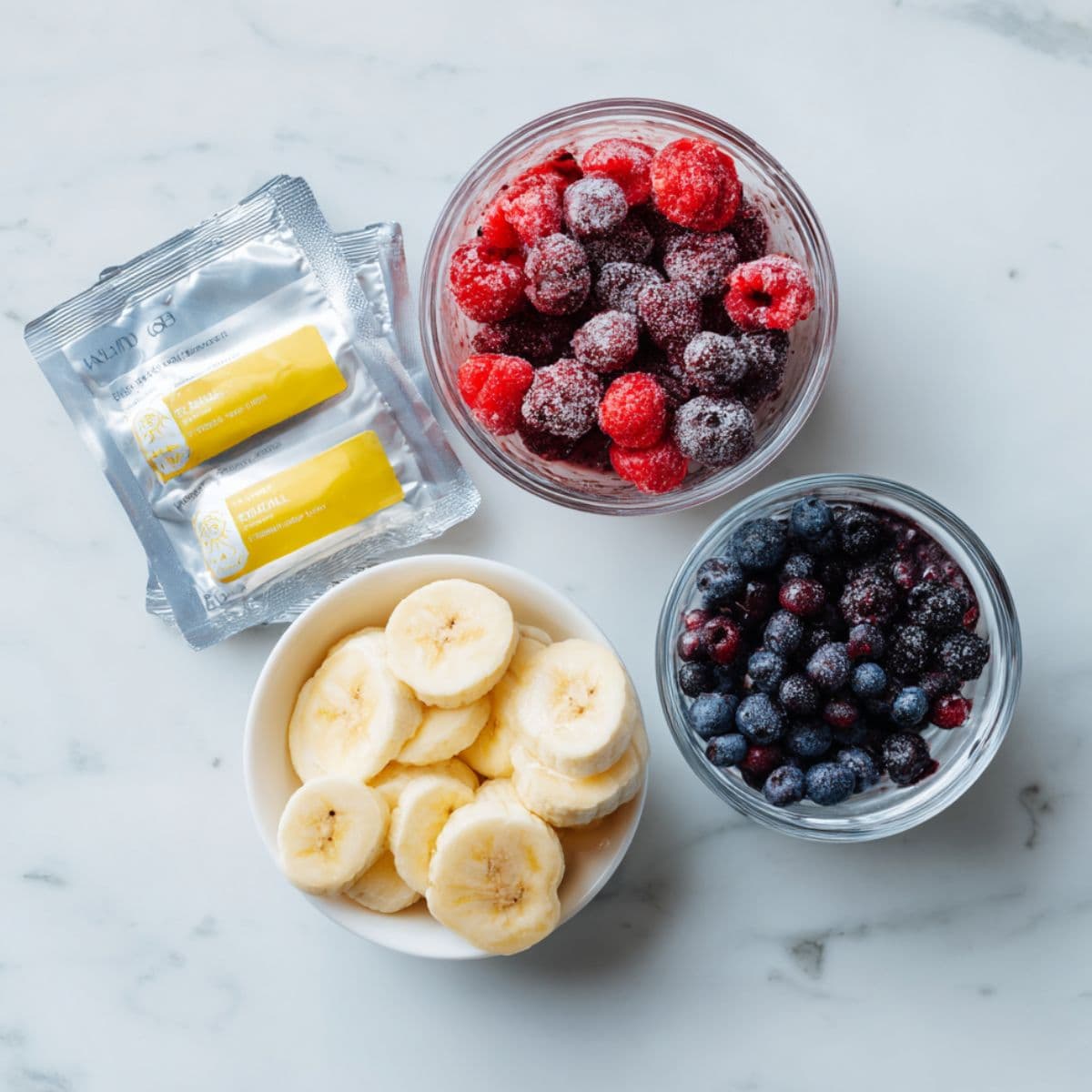 frozen acai packets, banana slices, mixed berries, and a small glass of liquid