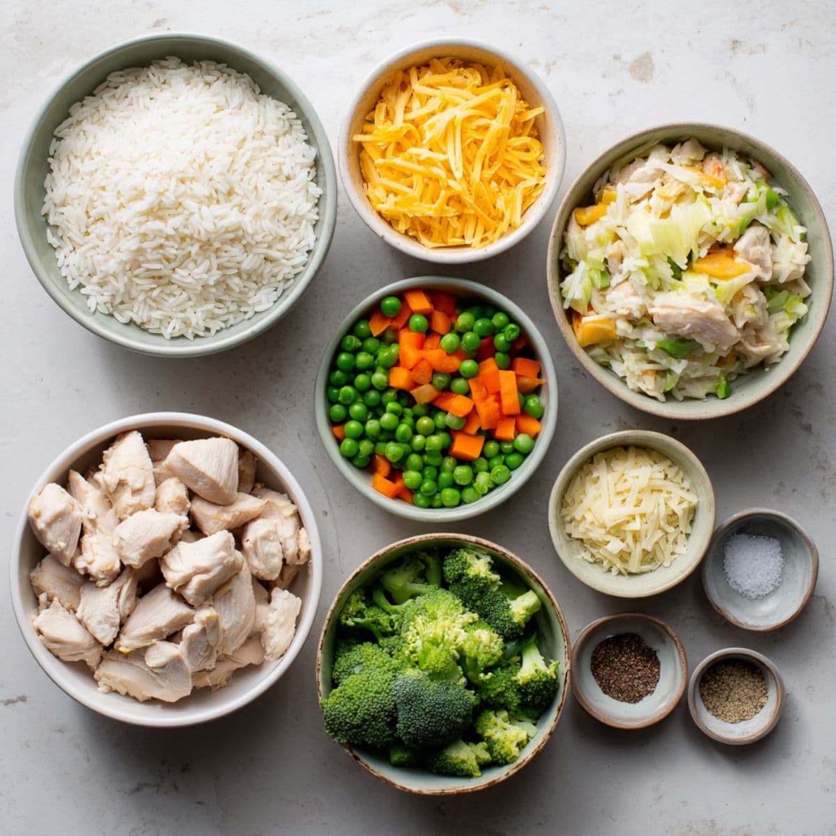 raw chicken, rice, cheese, vegetables, and seasonings arranged on a table