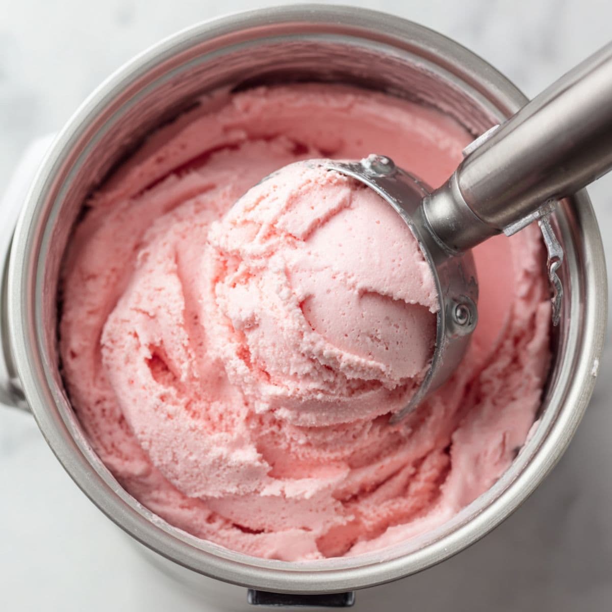 strawberry ice cream mixture forming soft peaks while churning in an ice cream maker with a pre-chilled container nearby