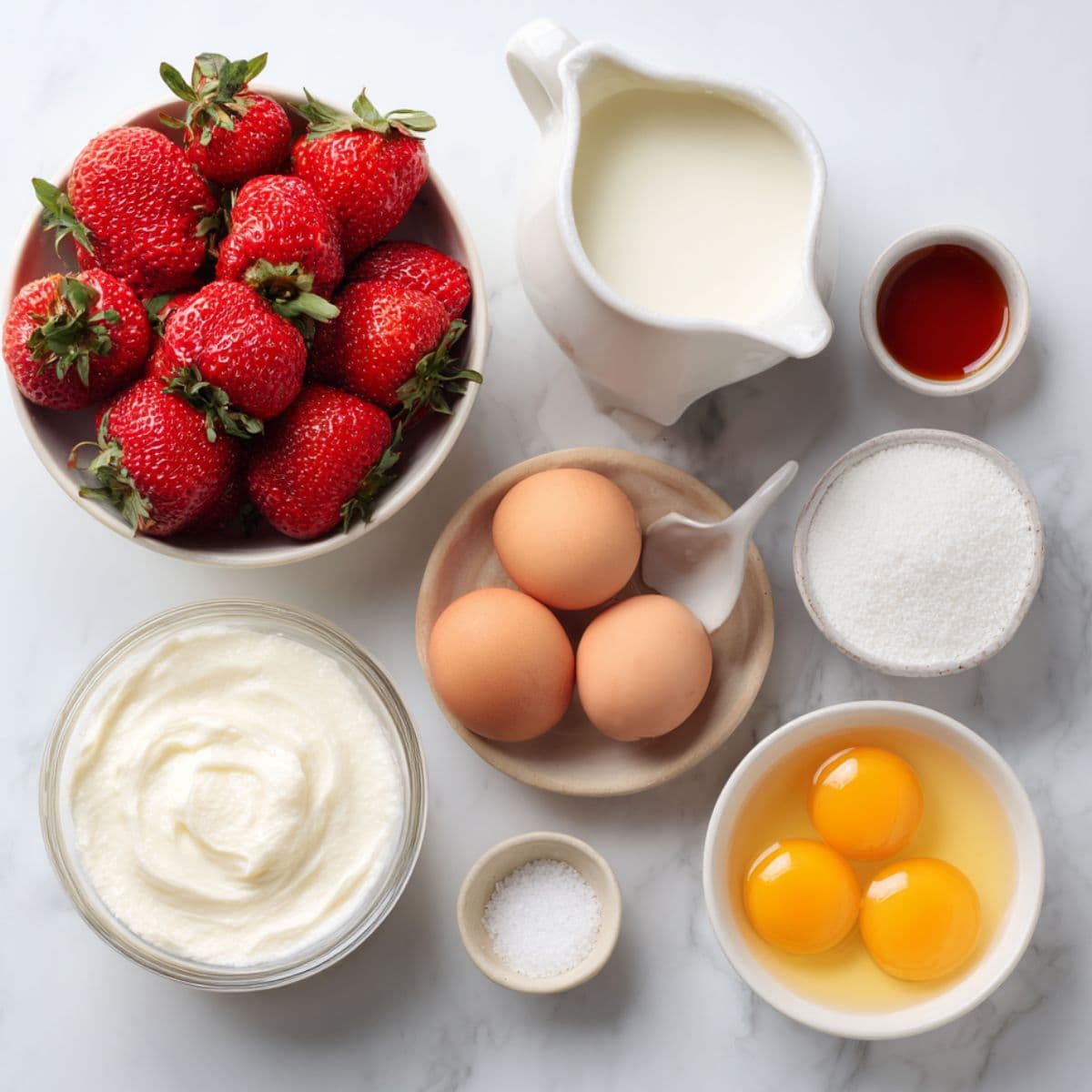 fresh strawberries, heavy cream, whole milk, egg yolks, sugar, vanilla extract, and salt arranged neatly on a white marble background