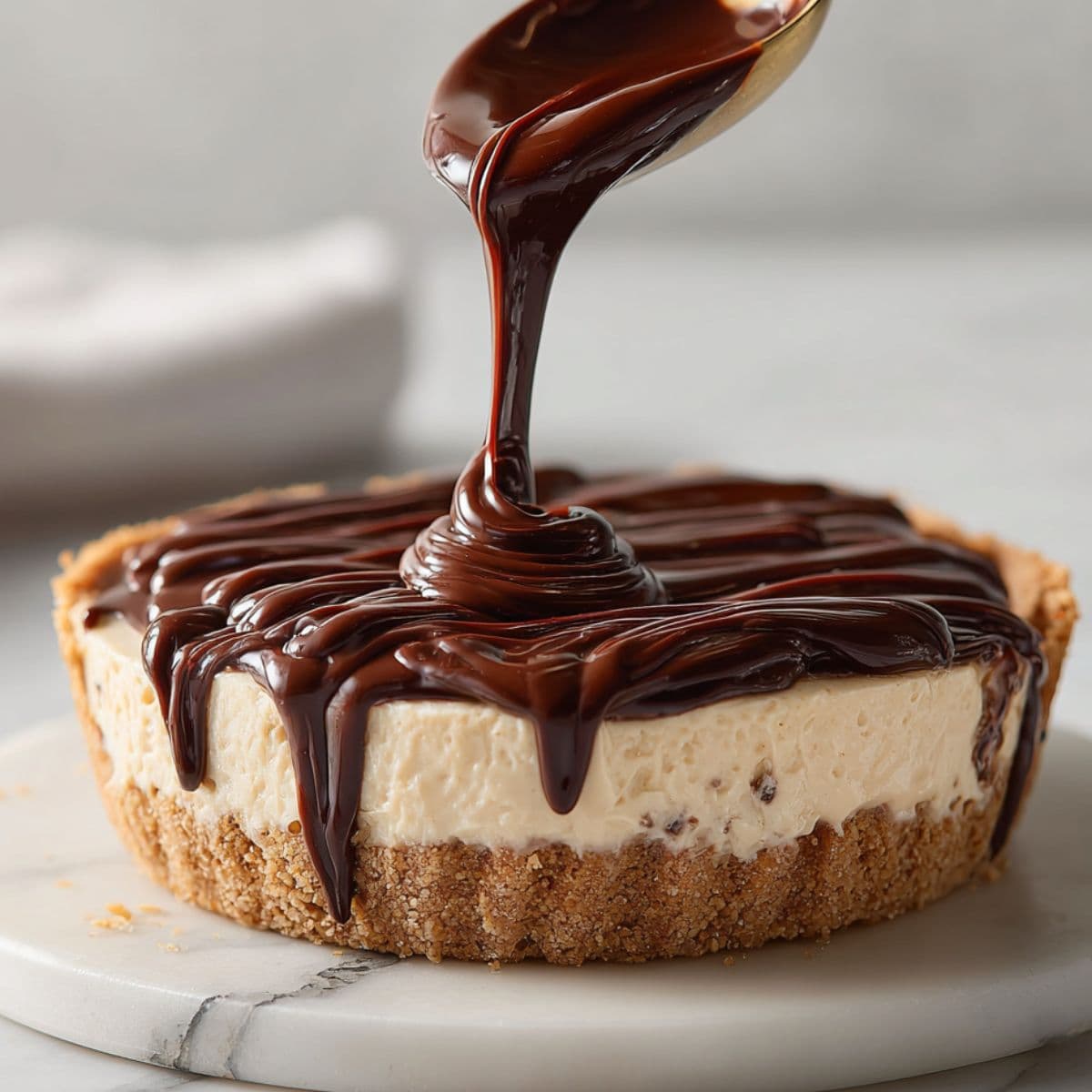 spoon pouring glossy chocolate ganache over chilled peanut butter pie with graham crust