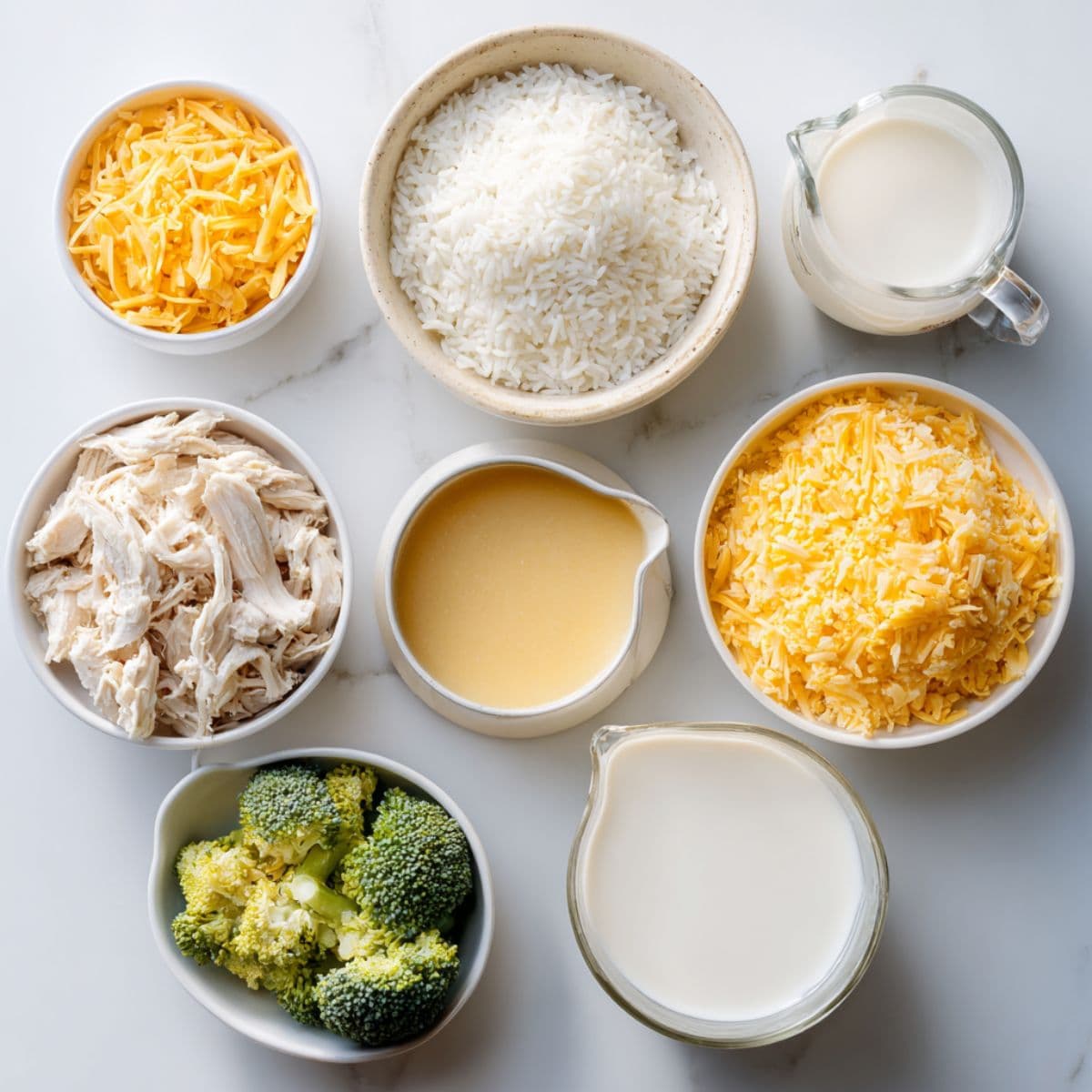 top view of ingredients for cheesy chicken broccoli rice casserole including shredded chicken, rice, broccoli, cheese, sour cream, and soup on a kitchen counter