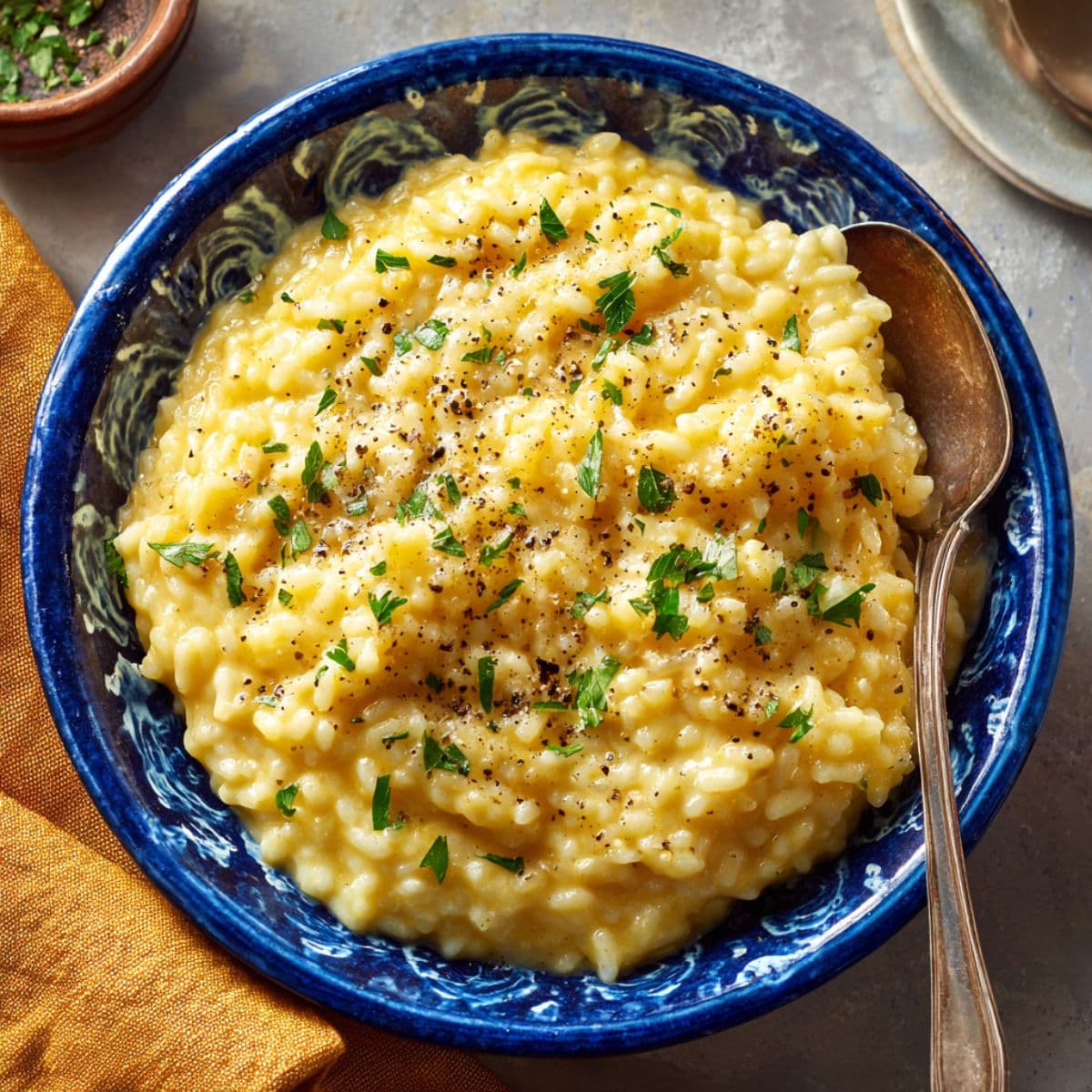 bowl of creamy pastina sprinkled with herbs and black pepper with a spoon resting inside