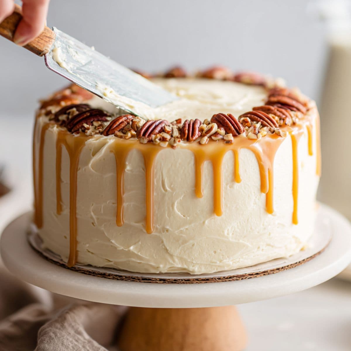 close-up of butter pecan cake being frosted with cream cheese frosting and topped with toasted pecans