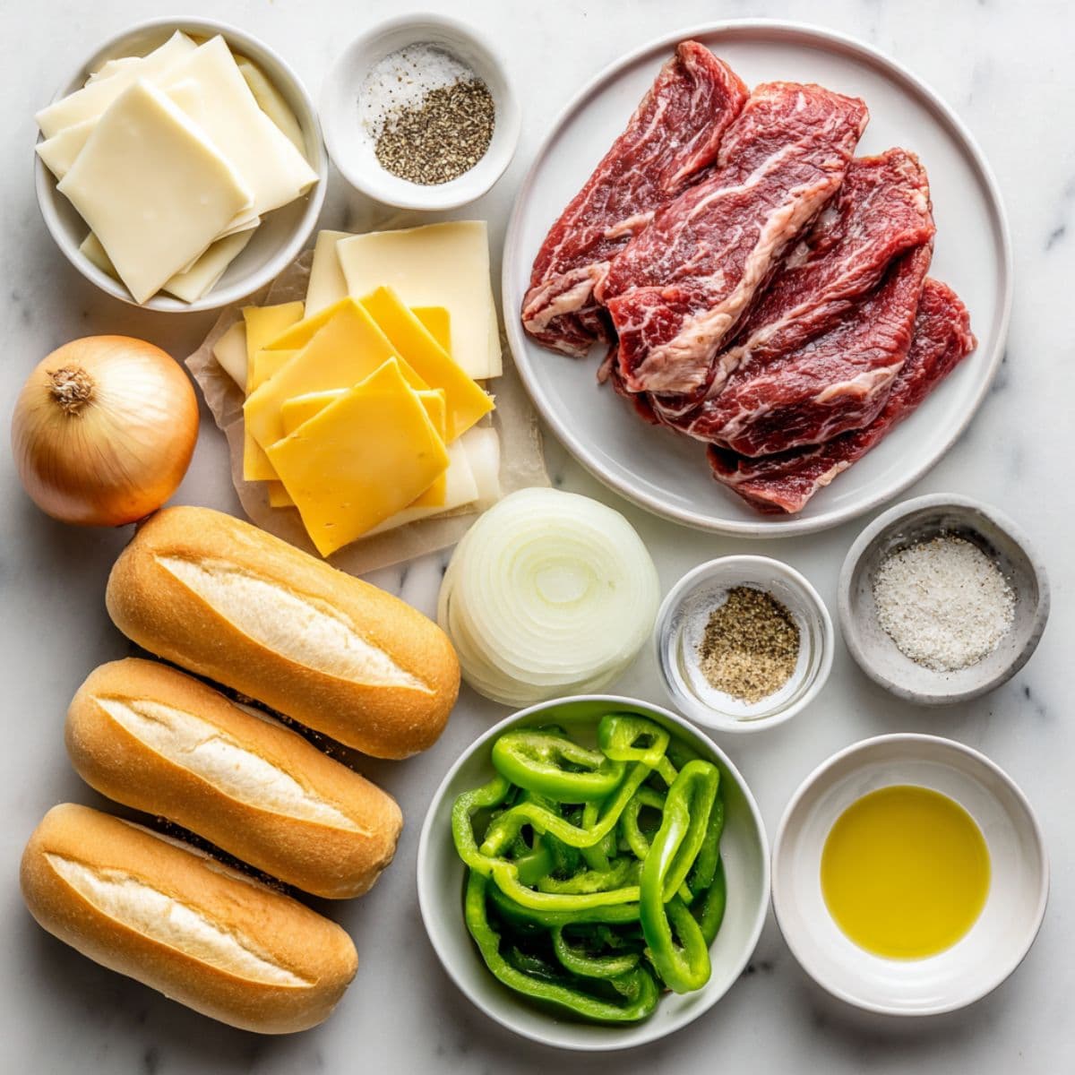 overhead view of ribeye steak, hoagie rolls, provolone cheese, onions, green bell peppers, and seasonings on white marble