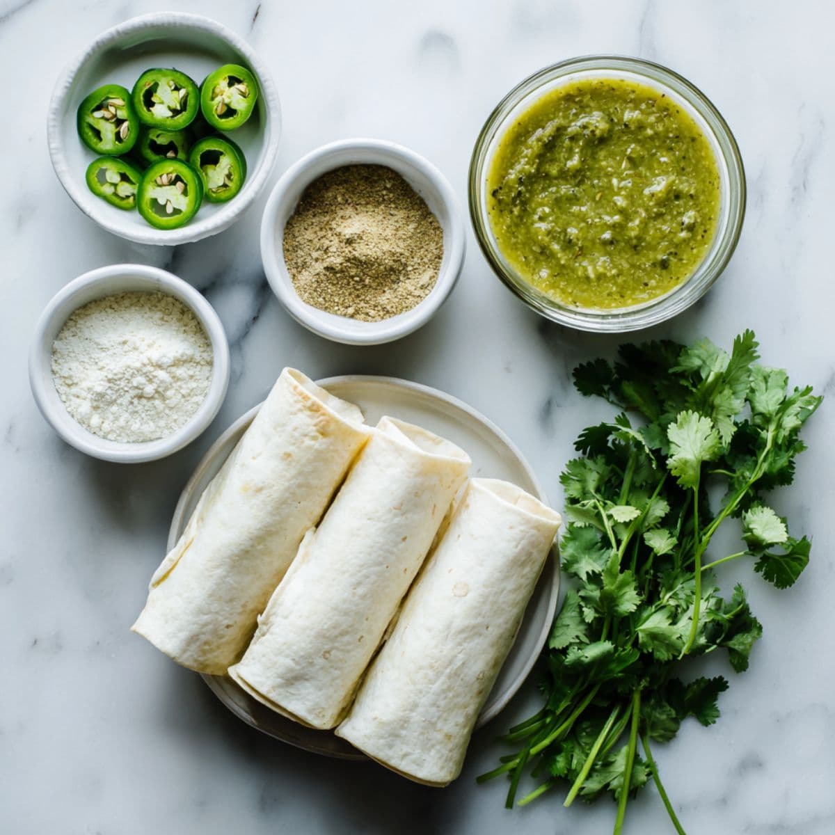 flat lay of white chicken enchiladas ingredients — garlic powder, cumin, onion powder, green enchilada sauce, jalapeños, and cilantro on a white background