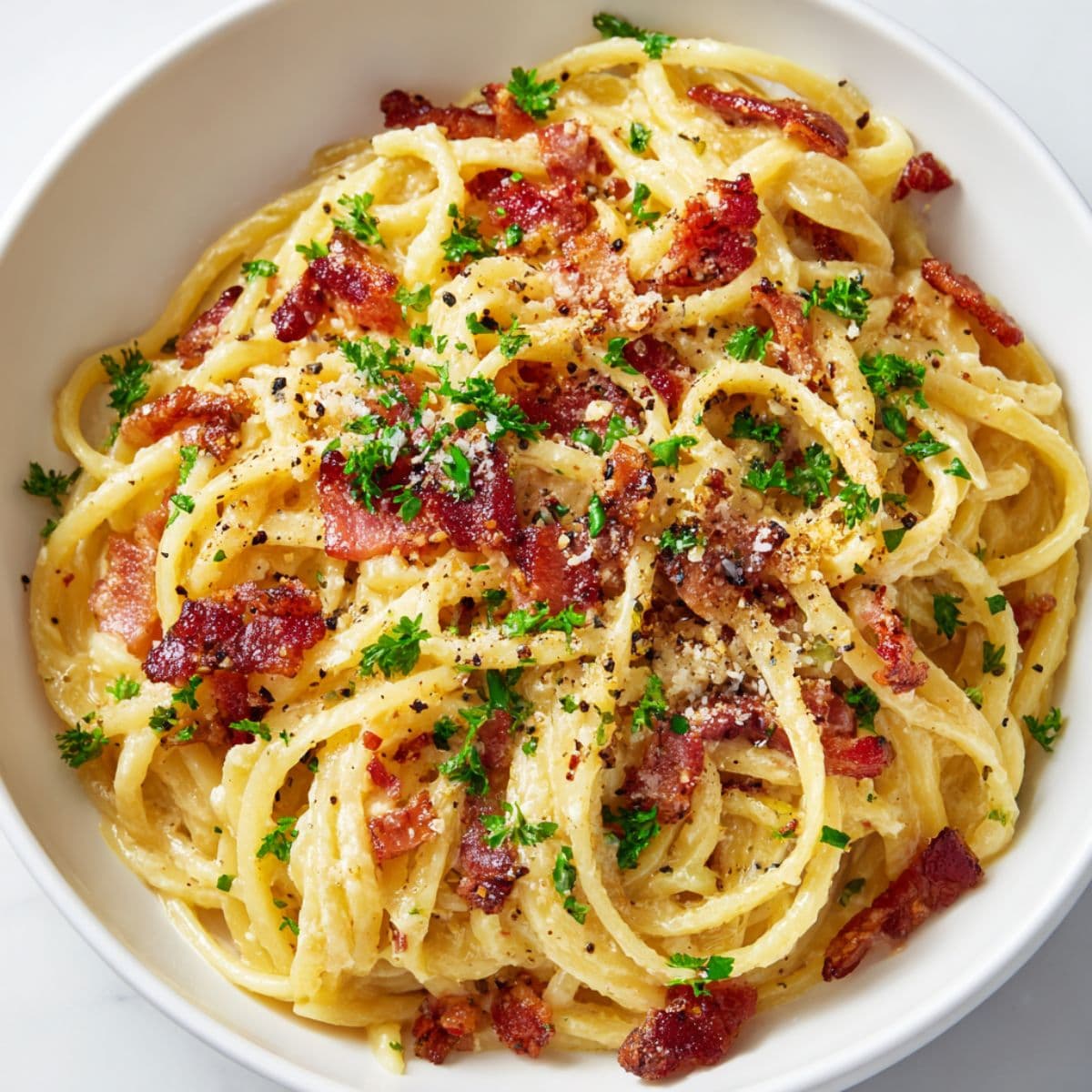 tossing bacon carbonara pasta in creamy sauce